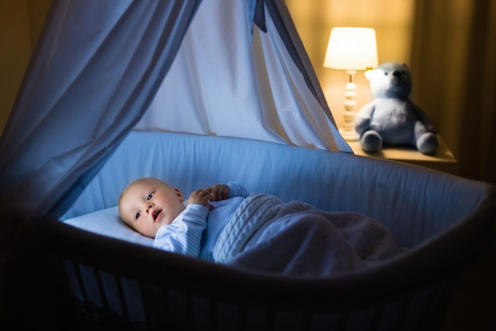 Auf dem Bild ist ein Baby zu sehen, das nachts in seinem Bettchen liegt. Das Baby ist wach.